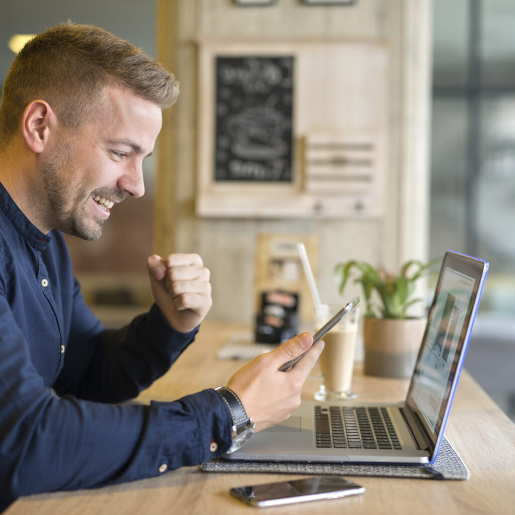 Happy customer with cellphone and laptop computer in coffee shop feeling lucky with an affordable SEO company in New-York